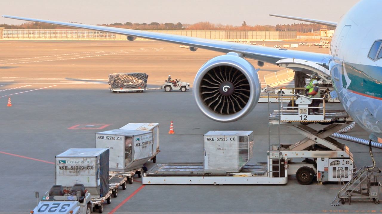 Luftfracht wird auf ein Flugzeug verladen, mit einem großen Triebwerk im Vordergrund.
