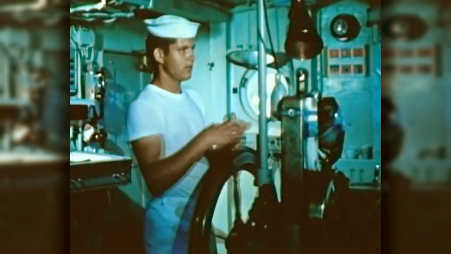 Ein Matrose in weißer Uniform steht in einem Maschinenraum und arbeitet an einem technischen Gerät.