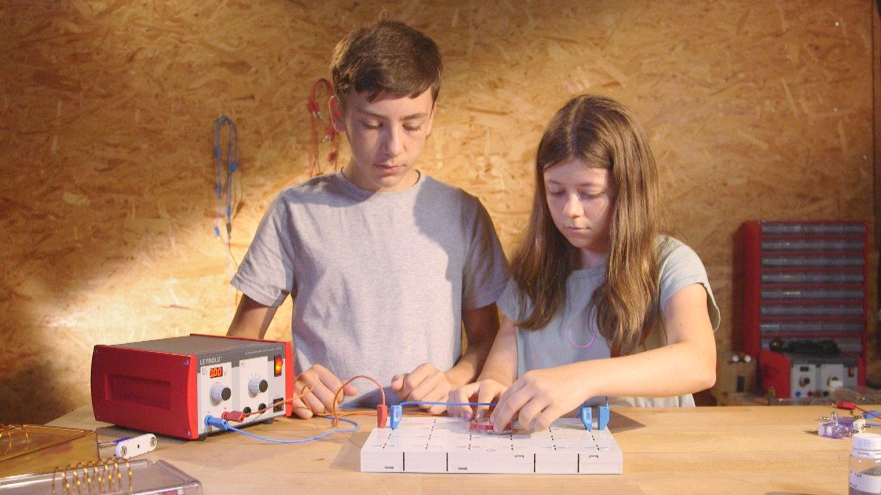 Zwei Kinder arbeiten an einem Experiment mit elektrischen Bauteilen auf einem Tisch.