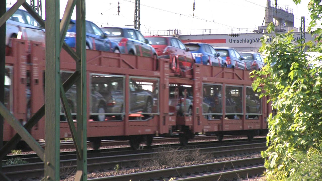 Ein Zug mit Autotransportwagen, beladen mit neuen Autos, fährt entlang der Gleise.
