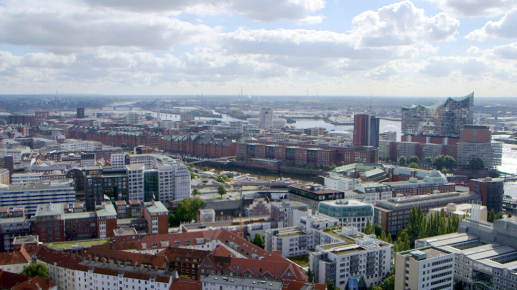 Luftaufnahme von Hamburg mit Hafen, modernen Gebäuden und Wolken am Himmel.