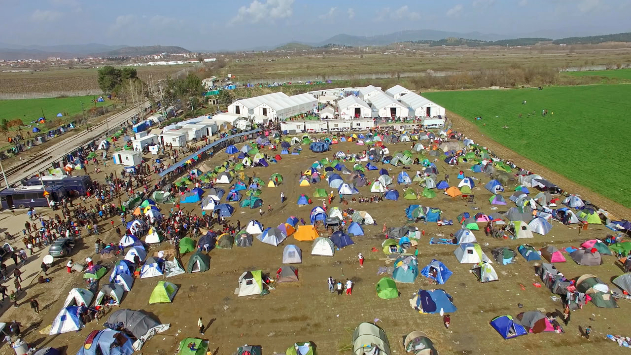 Luftaufnahme eines großen Flüchtlingslagers mit zahlreichen Zelten und Menschen auf einem offenen Feld.