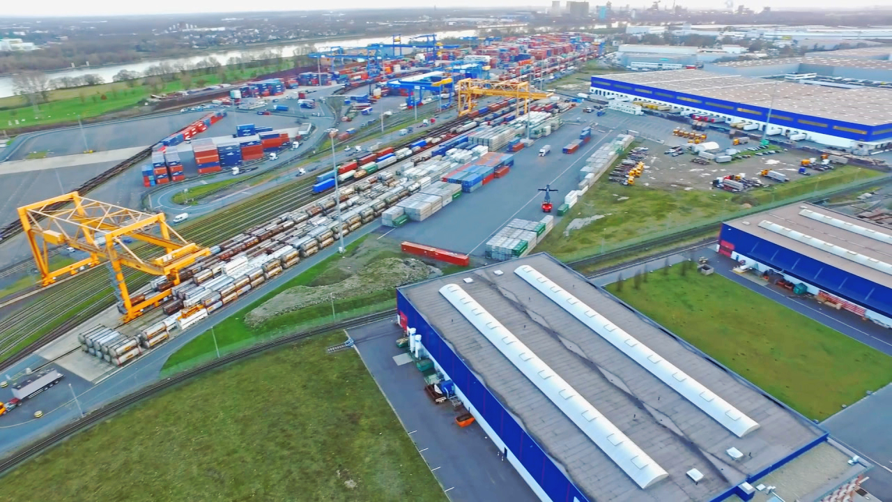 Luftaufnahme eines großen Containerhafens mit zahlreichen Containerschiffen und Lagerhäusern.