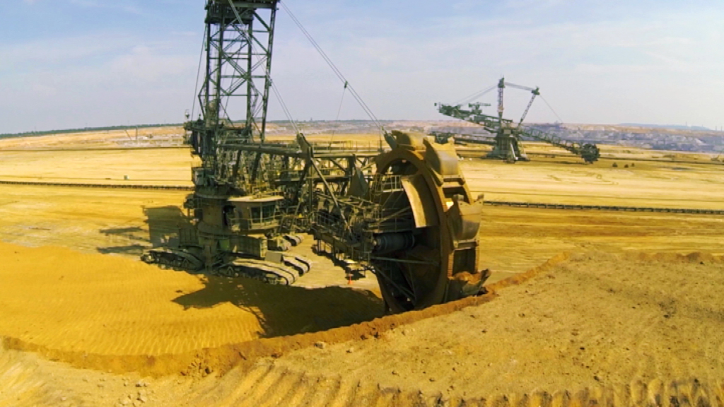 Ein großer Bagger im Tagebau, der Erde abträgt, mit einer weitläufigen Landschaft im Hintergrund.