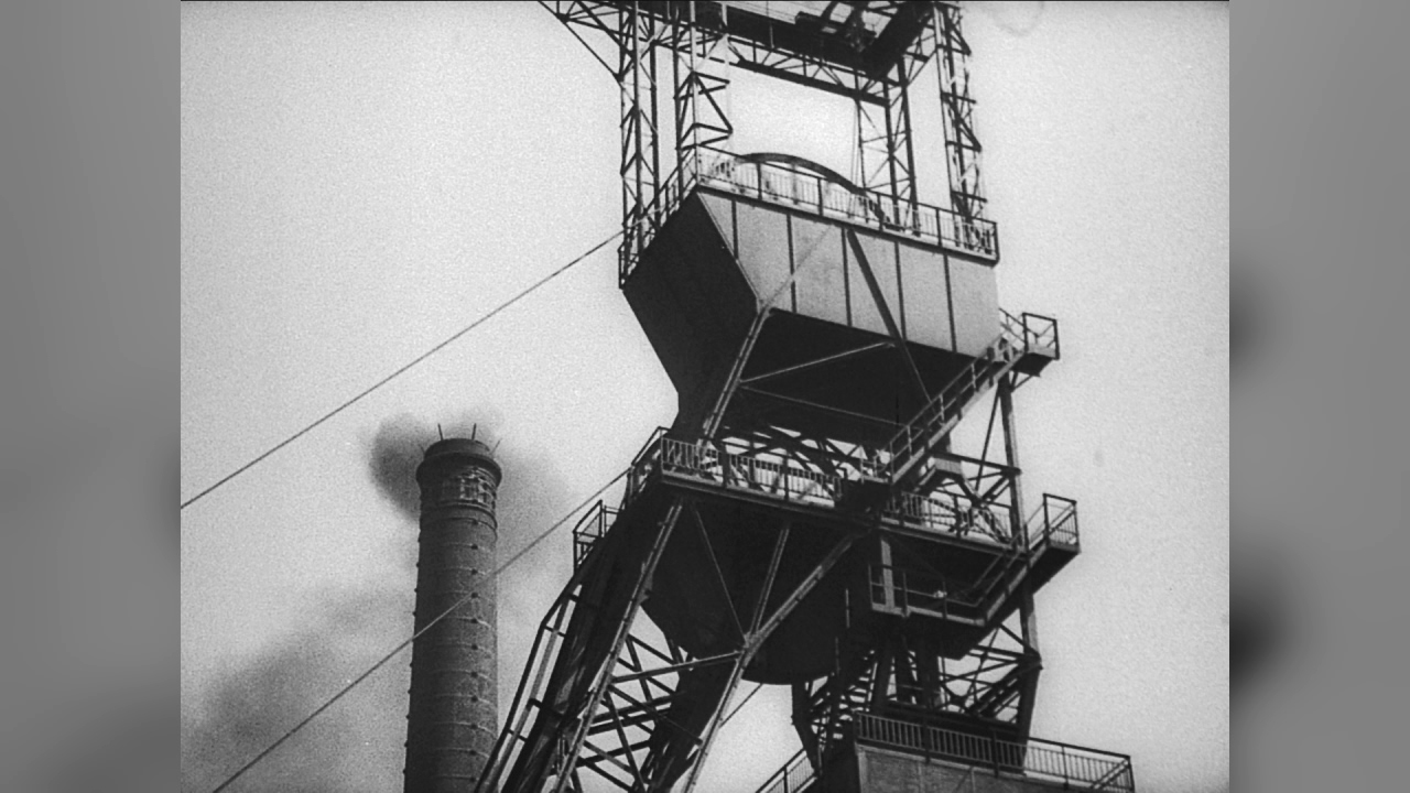 Eine industrielle Struktur mit einem Förderturm und einem Schornstein im Hintergrund.